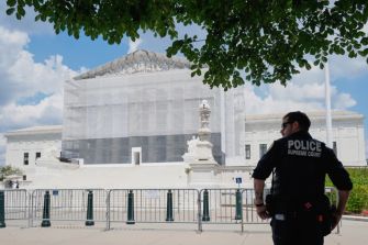 A police officer stands guard outside the U.S. Supreme Court building, which is covered in scaffolding.