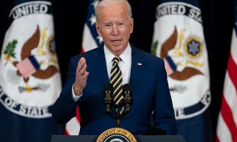 President Biden speaking at a podium with the presidential seal, addressing issues related to racism and xenophobia against Asian Americans, with flags in the background.