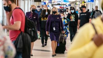 Passengers and airline staff in an airport terminal, many wearing masks, as they navigate through the busy space.