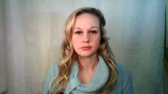 Rebekah Jones speaking during an online video, wearing a blue sweater against a neutral background.