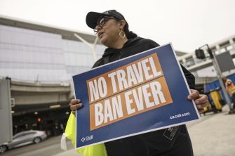 A person holding a sign that reads "NO TRAVEL BAN EVER" at an airport demonstration against travel restrictions.