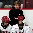 A woman stands behind hockey players on the bench during a game, appearing concerned or contemplative. A woman stands behind hockey players on the bench during a game, appearing concerned or contemplative.