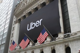 Exterior view of the New York Stock Exchange featuring a large Uber banner and American flags.