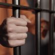 A close-up of a person's hands gripping prison bars, symbolizing incarceration. A close-up of a person's hands gripping prison bars, symbolizing incarceration.