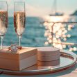 A engagement ring placed on a tray with two glasses of champagne, set against a scenic waterfront background. A engagement ring placed on a tray with two glasses of champagne, set against a scenic waterfront background.