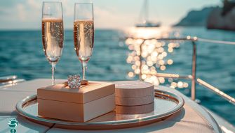 A engagement ring placed on a tray with two glasses of champagne, set against a scenic waterfront background.