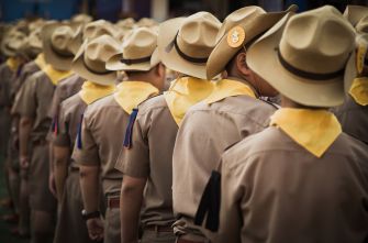 A group of boys in uniform and hats standing in line, with some wearing yellow neckerchiefs.