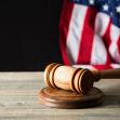 An image of a gavel on a wooden table, with an American flag partially visible in the background. An image of a gavel on a wooden table, with an American flag partially visible in the background.