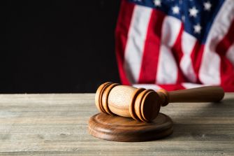 An image of a gavel on a wooden table, with an American flag partially visible in the background.