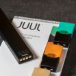 Image of a JUUL vaping device alongside flavored vape pods on a dark surface. Image of a JUUL vaping device alongside flavored vape pods on a dark surface.