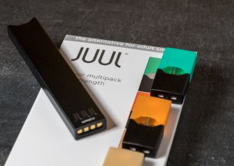 Image of a JUUL vaping device alongside flavored vape pods on a dark surface.