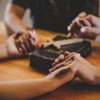 Hands clasped in prayer over a Bible on a wooden table. Hands clasped in prayer over a Bible on a wooden table.