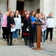 A group of athletes and supporters protesting for women's sports rights outside a government building, holding signs advocating for fair play and the protection of women's sports. A group of athletes and supporters protesting for women's sports rights outside a government building, holding signs advocating for fair play and the protection of women's sports.