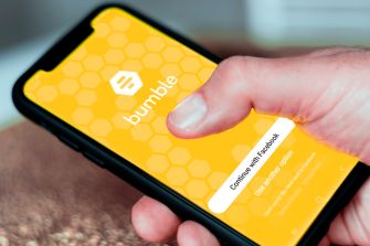 A person holding a smartphone displaying the Bumble app's login screen.