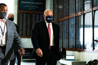 Postmaster General Louis DeJoy arriving at a government building, accompanied by two individuals, while wearing a mask.
