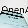 A smartphone displaying the ChatGPT interface in front of an OpenAI logo. A smartphone displaying the ChatGPT interface in front of an OpenAI logo.