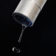 A close-up of a faucet dripping water against a dark background. A close-up of a faucet dripping water against a dark background.