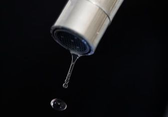 A close-up of a faucet dripping water against a dark background.