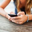 A person using a smartphone while sitting at a wooden table. A person using a smartphone while sitting at a wooden table.