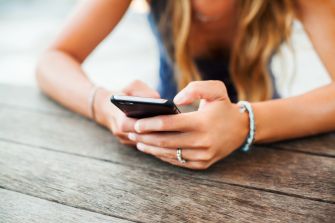 A person using a smartphone while sitting at a wooden table.