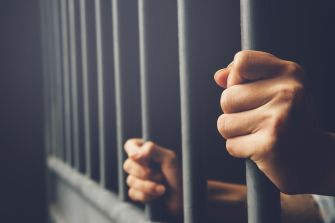 A close-up of hands gripping jail cell bars, symbolizing confinement and lack of support.
