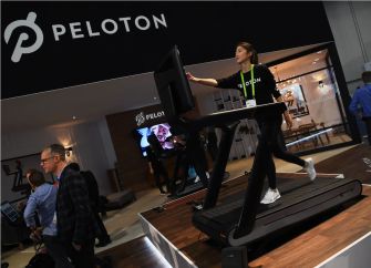 Peloton treadmill on display at a fitness expo with a woman demonstrating its use.