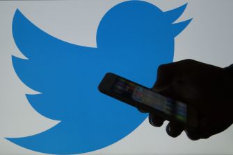 Silhouette of a hand holding a smartphone in front of a large Twitter logo.