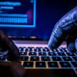 Gloved hands typing on a laptop keyboard, possibly indicating hacking activities. Gloved hands typing on a laptop keyboard, possibly indicating hacking activities.