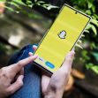 A person holding a smartphone displaying the Snapchat logo on its screen. A person holding a smartphone displaying the Snapchat logo on its screen.