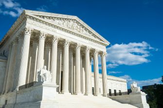 Exterior view of the United States Supreme Court building under a blue sky with clouds.