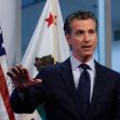 California Governor Gavin Newsom speaking at a press conference with American and California flags in the background. California Governor Gavin Newsom speaking at a press conference with American and California flags in the background.