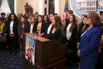 A group of women standing together at a press conference advocating for survivors' rights, with a banner reading "Justice for Survivors" in front of them.