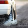 A close-up view of a white car's rear tire leaving smoke and debris on a racing surface during a drag race. A close-up view of a white car's rear tire leaving smoke and debris on a racing surface during a drag race.