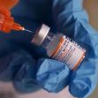 Close-up of a gloved hand holding a COVID-19 vaccine vial with a syringe poised to draw the vaccine. Close-up of a gloved hand holding a COVID-19 vaccine vial with a syringe poised to draw the vaccine.