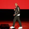 Dave Chappelle performing on stage during a live comedy show. Dave Chappelle performing on stage during a live comedy show.