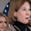 Image of Sidney Powell speaking at a press conference, with flags in the background. Image of Sidney Powell speaking at a press conference, with flags in the background.