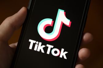A person holding a smartphone displaying the TikTok logo on the screen.
