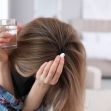 A woman holding a glass of water and a pill, looking distressed. A woman holding a glass of water and a pill, looking distressed.