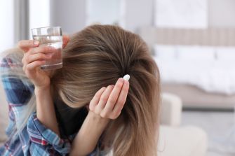 A woman holding a glass of water and a pill, looking distressed.