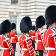 A group of British soldiers in traditional uniforms with bearskin hats standing in formation outside a historic building. A group of British soldiers in traditional uniforms with bearskin hats standing in formation outside a historic building.