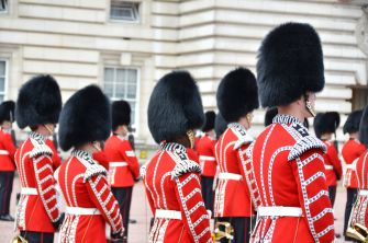 A group of British soldiers in traditional uniforms with bearskin hats standing in formation outside a historic building.