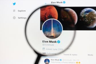 Elon Musk's Twitter profile page displayed on a computer screen, magnified through a lens.