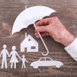 A hand holding a paper umbrella over cut-out figures of a family, a house, and a car, symbolizing insurance protection. A hand holding a paper umbrella over cut-out figures of a family, a house, and a car, symbolizing insurance protection.
