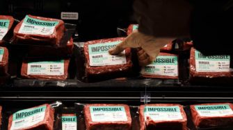 A hand pointing at packages of Impossible Burger displayed in a grocery store.