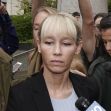 A woman surrounded by a crowd, appearing somber outside a courthouse. A woman surrounded by a crowd, appearing somber outside a courthouse.
