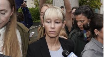 A woman surrounded by a crowd, appearing somber outside a courthouse.