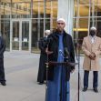 A group of men, including a speaker in traditional attire, addresses the media outside a courthouse, following the conviction of militia leader Michael Hari for a mosque bombing. A group of men, including a speaker in traditional attire, addresses the media outside a courthouse, following the conviction of militia leader Michael Hari for a mosque bombing.