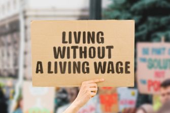 A person holding a sign that reads "LIVING WITHOUT A LIVING WAGE" at a protest or demonstration.