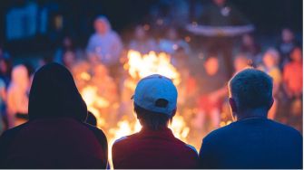 A group of children sitting around a campfire in a dark outdoor setting.