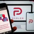 Image showing a smartphone displaying the Parler website alongside a large screen showcasing the Parler logo, emphasizing its branding as a free speech platform. Image showing a smartphone displaying the Parler website alongside a large screen showcasing the Parler logo, emphasizing its branding as a free speech platform.